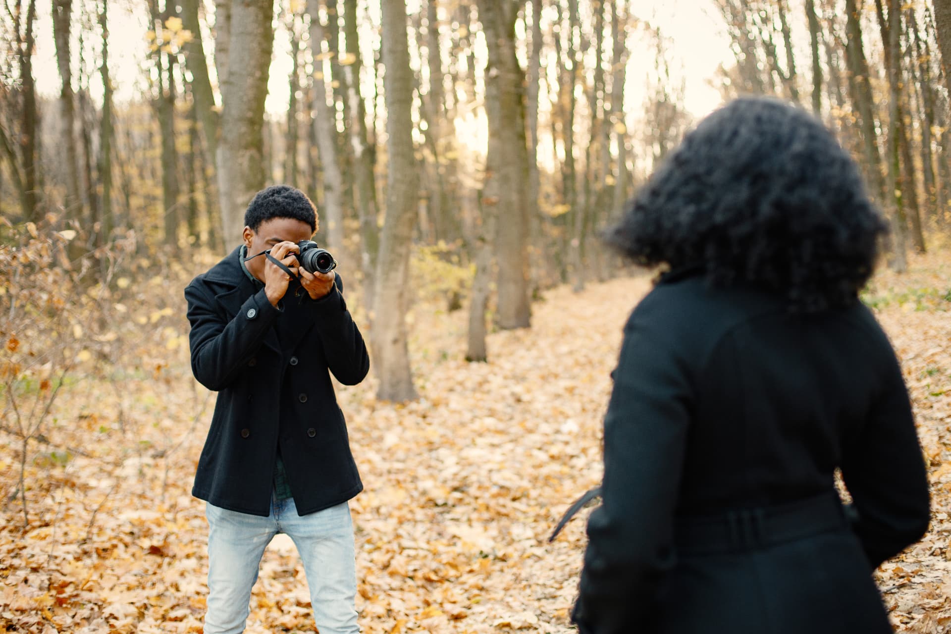 Photographer shooting a portrait of a woman on a leaf-covered path in an autumn wood.