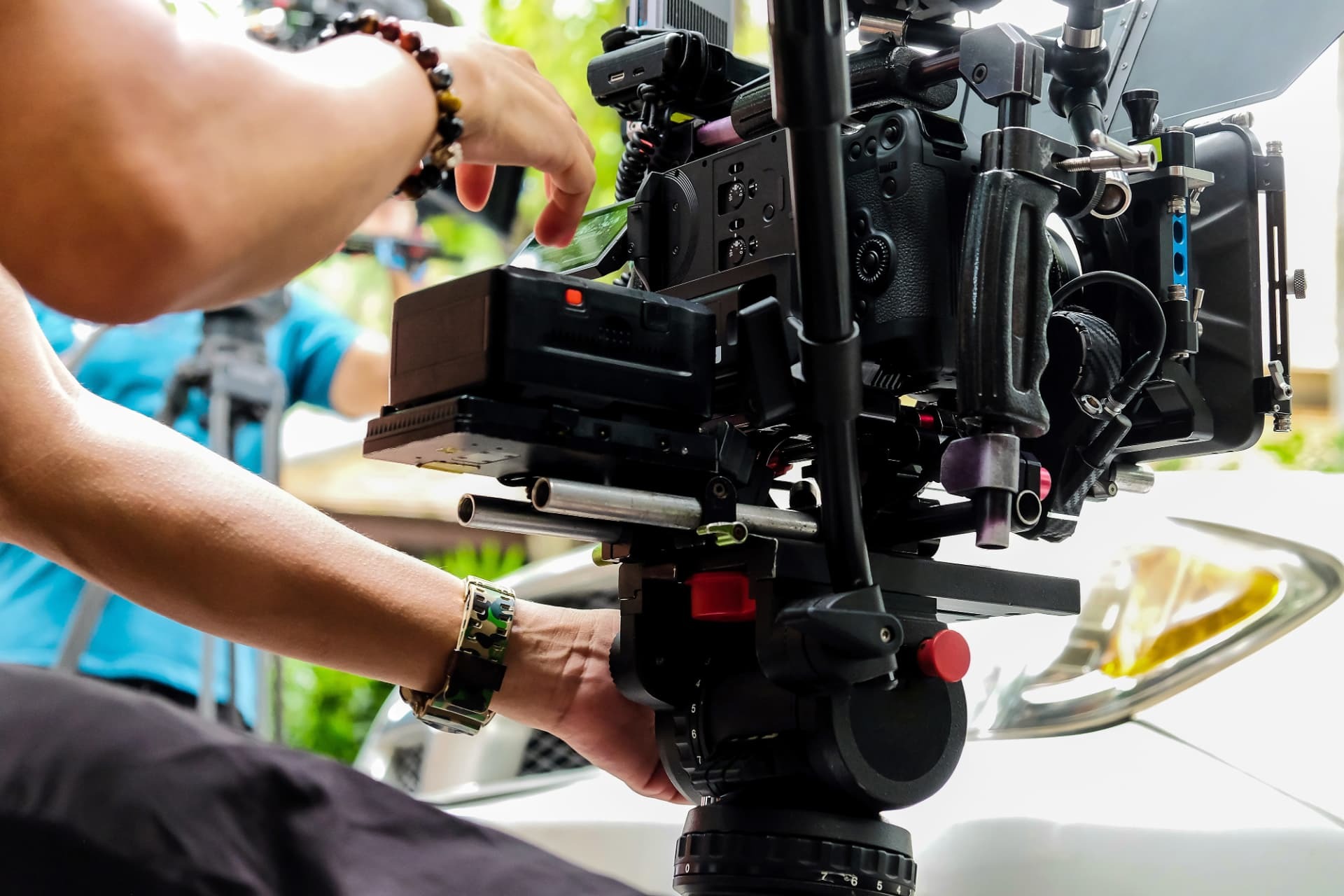 Camera operator's hands adjusting a rigged cinema camera on a fluid head during an outdoor shoot.