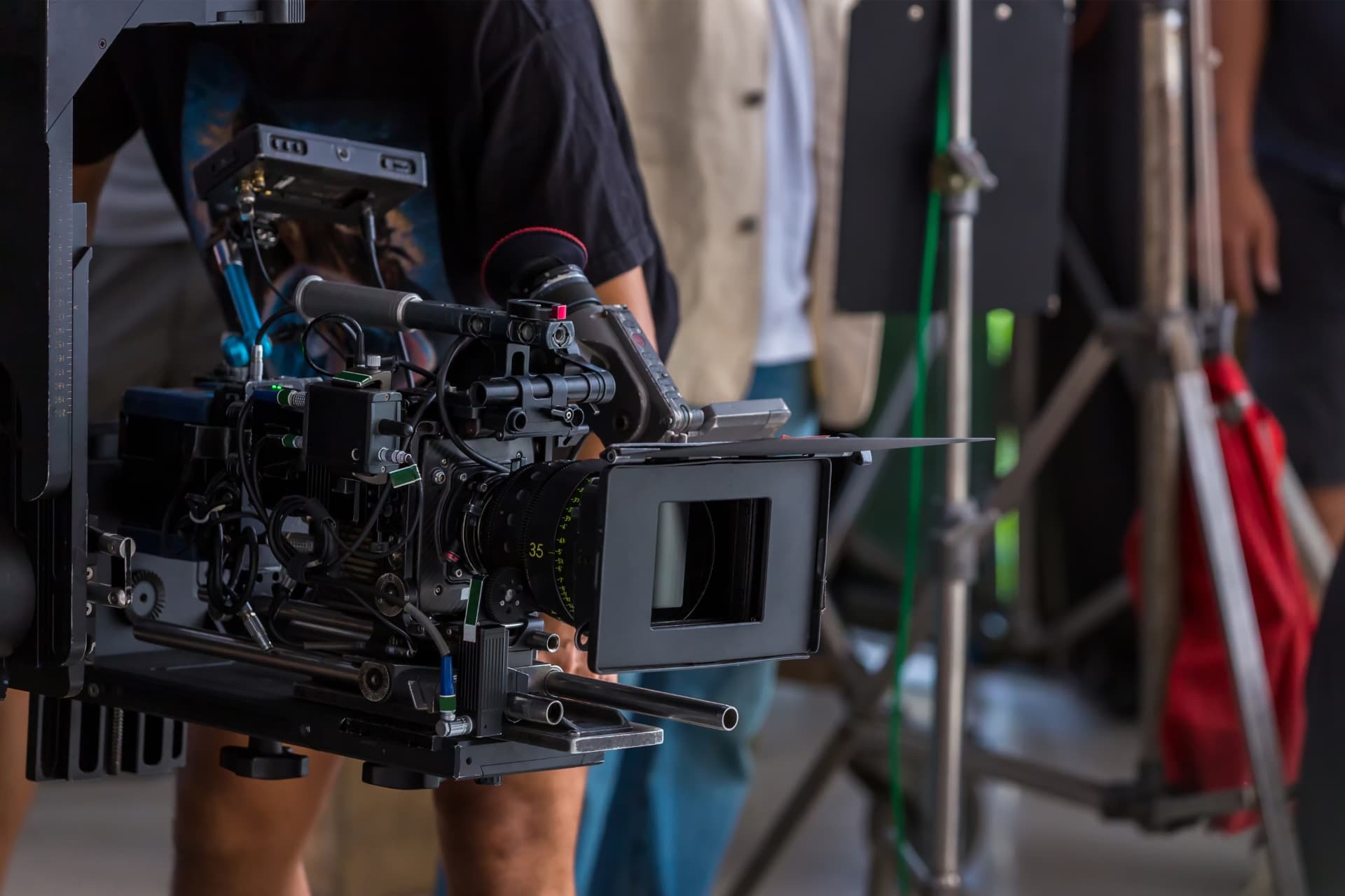 Cinema camera with a 35mm lens and matte box on set, crew and lighting stands behind.