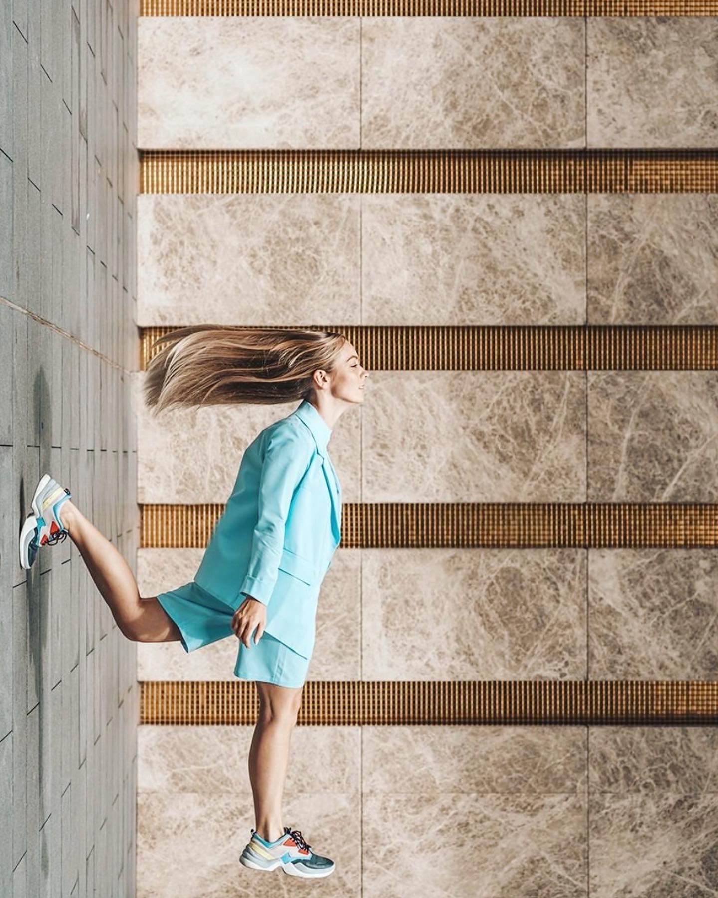 Model in a turquoise suit caught mid-stride against a marble and gold wall.