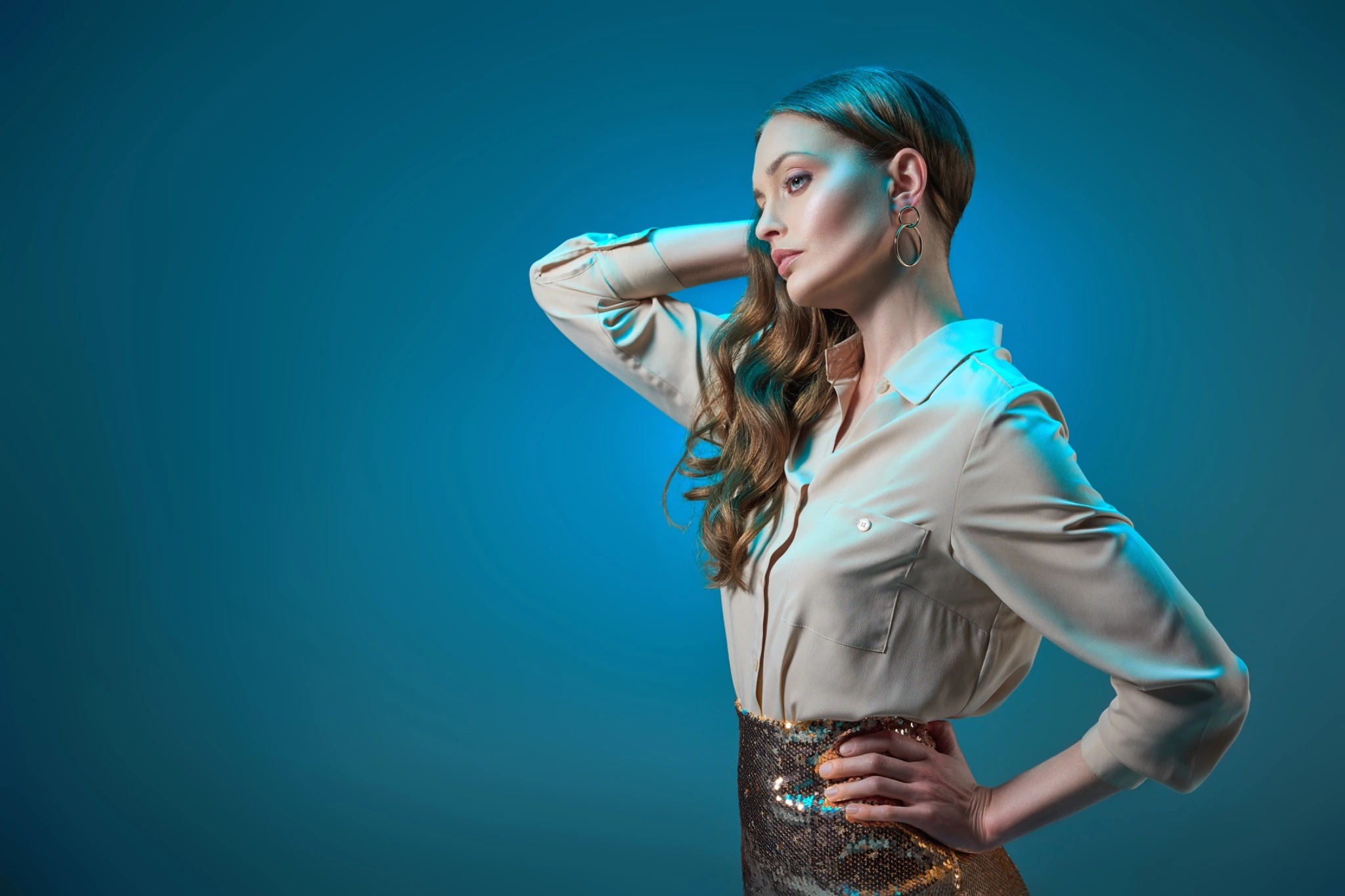 Woman in a satin blouse and sequined skirt posing against a teal background.