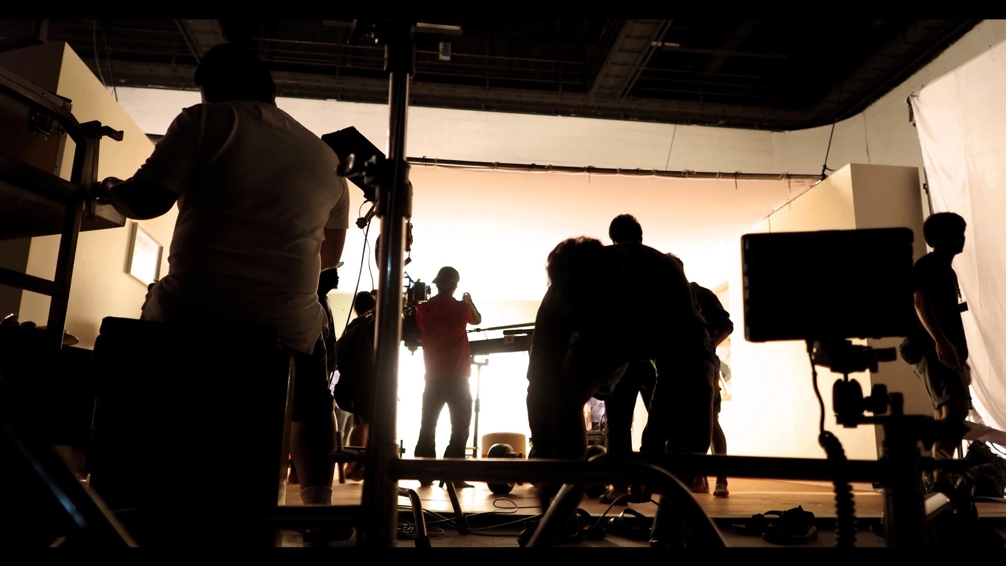 Silhouetted crew members and camera equipment in front of a brightly lit set.