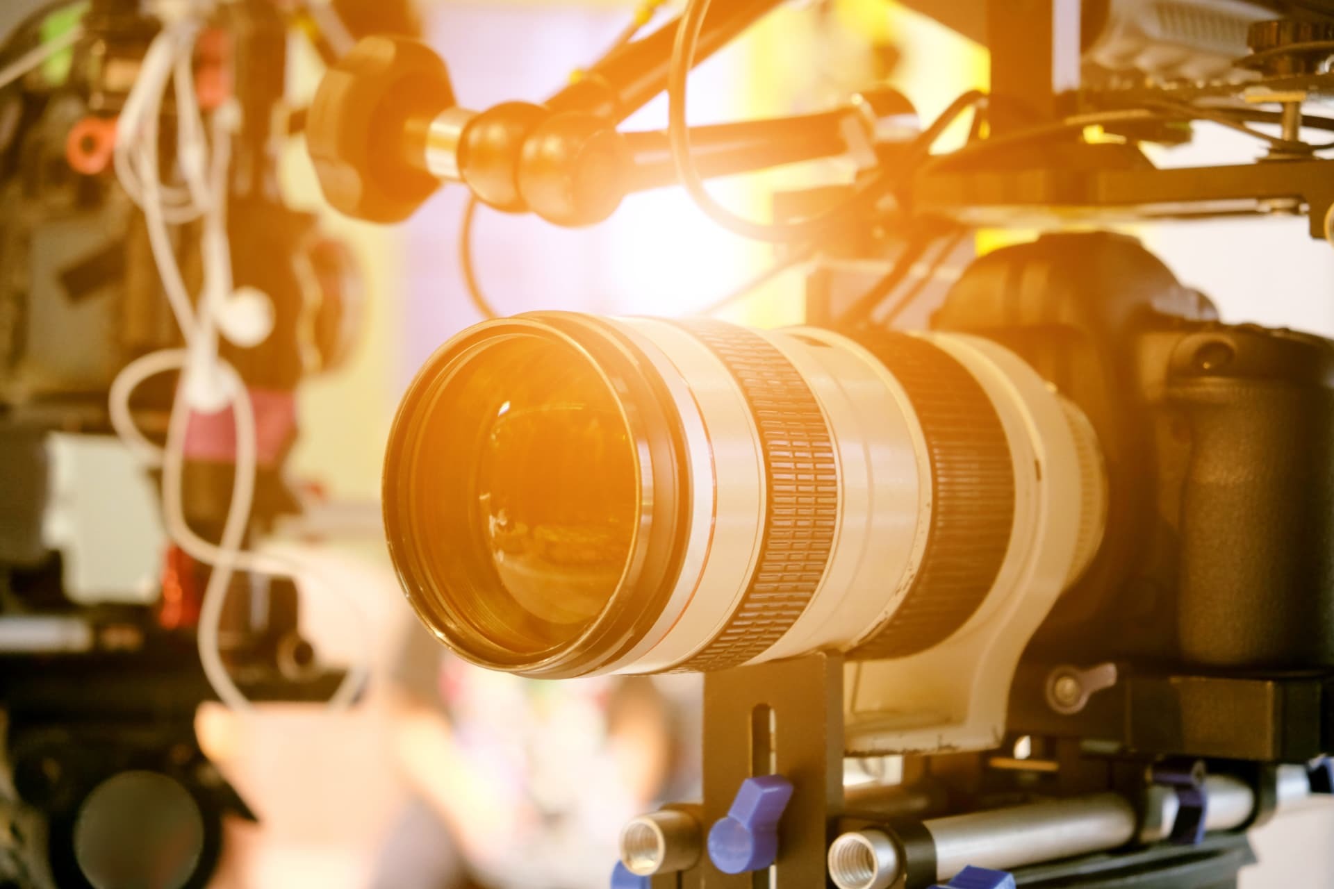 Close-up of a white telephoto lens on a camera rig, glowing in warm studio light.