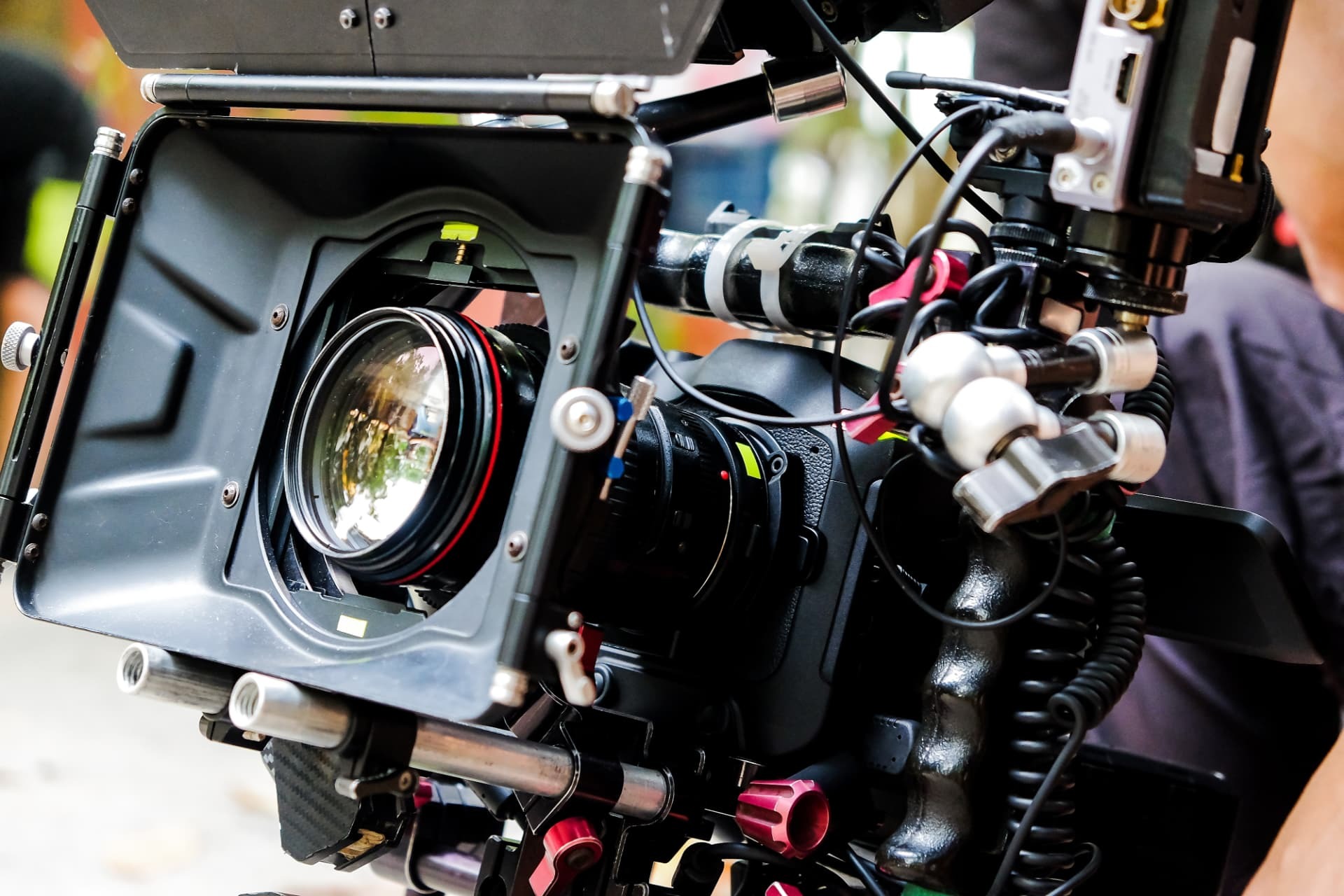Close-up of a cinema lens inside a matte box, with cables and red rig knobs.