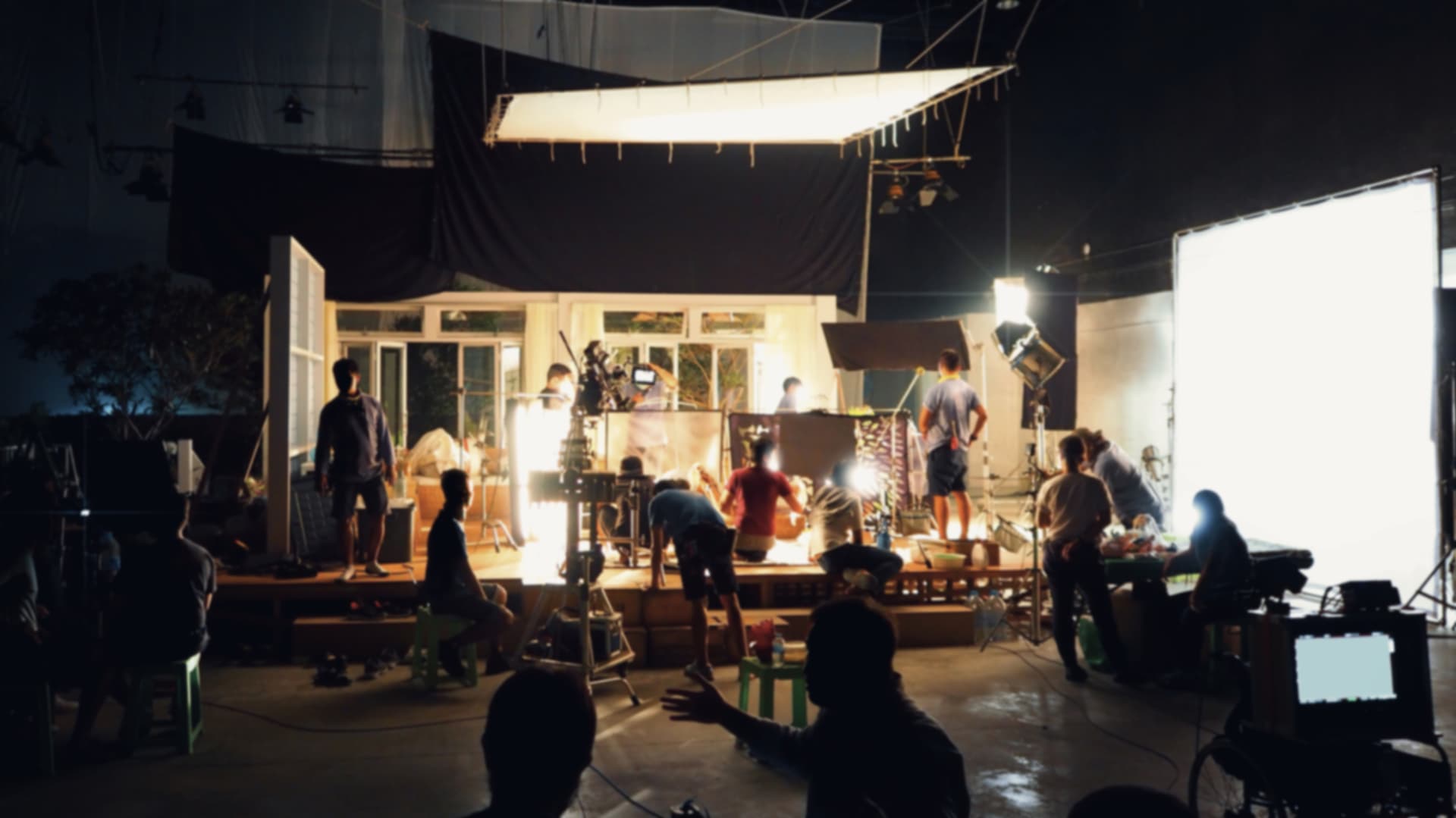 Film crew working a night shoot around a brightly lit set build.