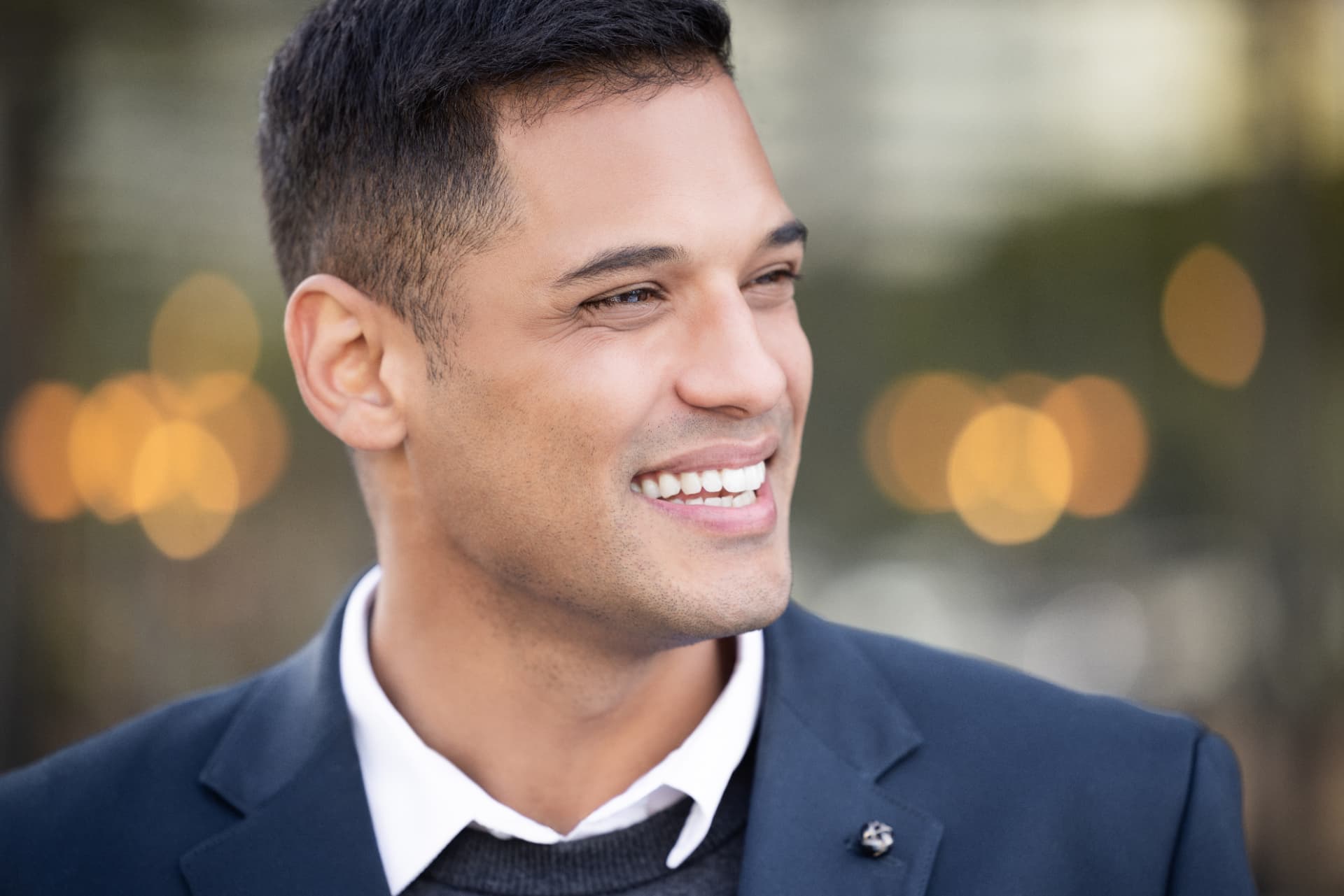 Smiling man in a navy blazer photographed against soft city lights.