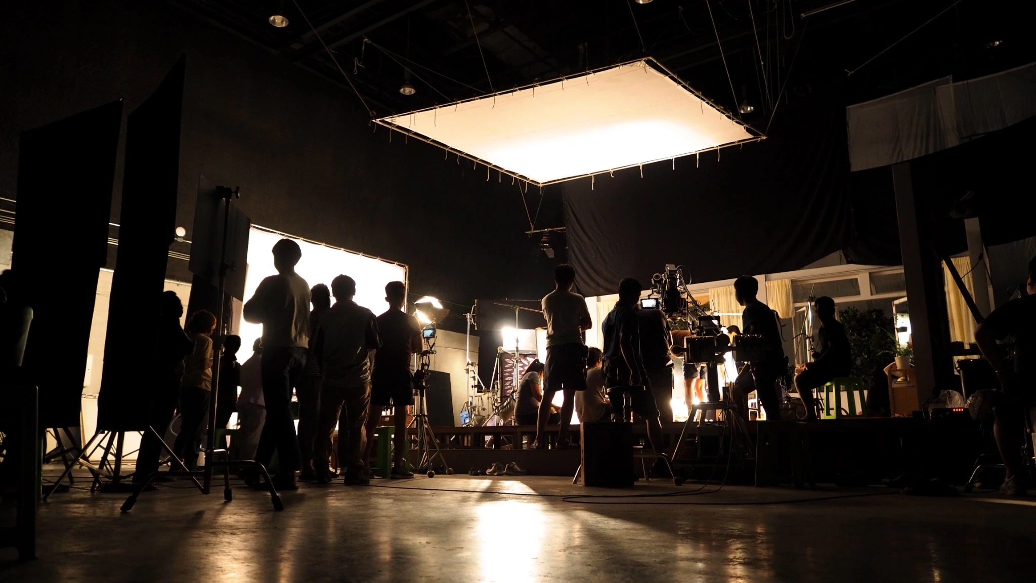 Wide view of a production crew working beneath large lights in a dark studio.