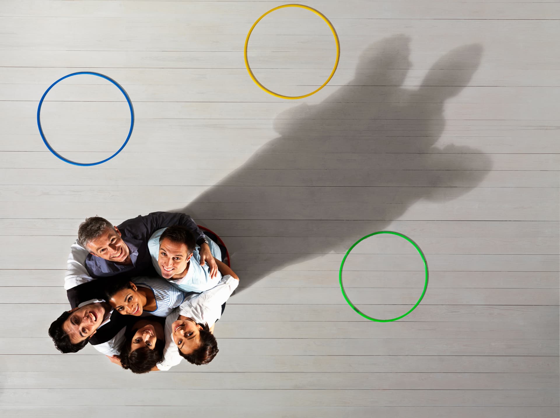 Overhead shot of a team huddled together on a pale floor marked with coloured circles.